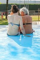 middle aged mom and young daughter dressing swimwear having fun with a tablet in a poolside photo