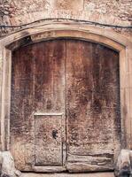 Brown wooden old door made from slats photo. Gray brick wall medieval house. Entrance with keyhole and iron fittings photo