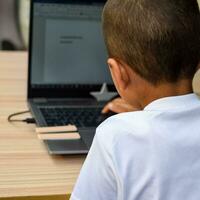 Little boy sitting at table using laptop for online class in Grade 1, Child studying on laptop from home for distance learning online education, School boy children lifestyle concept photo