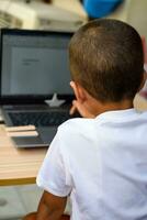 Little boy sitting at table using laptop for online class in Grade 1, Child studying on laptop from home for distance learning online education, School boy children lifestyle concept photo