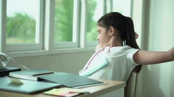 cansado pequeno menina , sentindo-me calibre para Faz lição de casaalongamento corpo e bocejando sentado às mesa dentro moderno dentro sala, Exausta criança estudante video