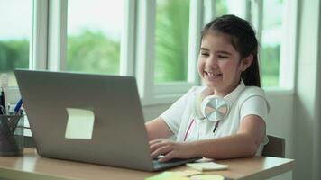 criança menina sorrir apreciar e-learning em computador caderno com para rir para engraçado comunicação e estude conectados ou aprender a partir de casa para jogar computador portátil de costas para escola video