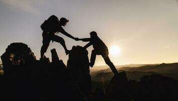 silueta de trabajo en equipo de tres excursionistas ayudándose unos a otros en la parte superior del equipo de montañismo. trabajo en equipo amistad caminatas ayudarse unos a otros confianza asistencia silueta en las montañas, amanecer. foto