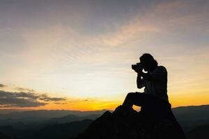 silueta de un fotógrafo en parte superior de un montaña a puesta de sol foto