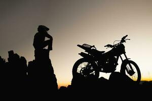 hombre con motocross bicicleta en contra hermosa luces, silueta de un hombre con motocross motocicleta en parte superior de rock alto montaña a hermosa atardecer, enduro motocicleta viaje concepto. foto