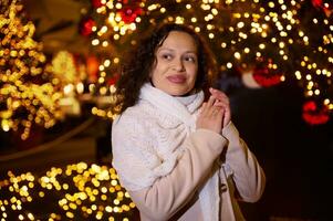 sonriente contento mujer caminando en Navidad mercado decorado con fiesta luces en el noche. sensación contento en grande ciudad. foto