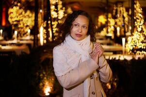 atractivo mujer con manos ahuecado, haciendo querido deseo para Navidad, en pie en el calle con hermosa iluminaciones foto