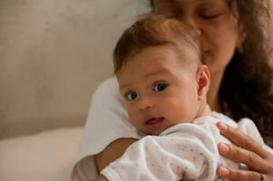 Authentic portrait of adorable baby boy looking at camera, while his mom hugging and holding him in her arms photo