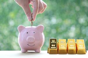 Woman hand putting a coin into piggy bank and gold bar on natural green background,Business investment and Saving money for prepare in future concept photo