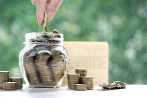 Finance, Woman hand putting a coin into glass bottle on nature green background,Business investment and Save money for prepare in future concept photo