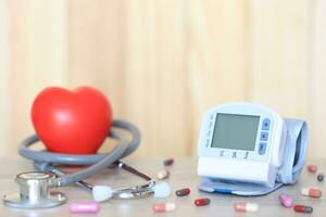 médico tonómetro para medición sangre presión con estetoscopio y rojo corazón en madera fondo, médico gastos y salud cuidado concepto foto