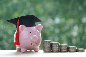 graduación sombrero en cerdito banco con apilar de monedas dinero en natural verde fondo, ahorro dinero para educación concepto foto