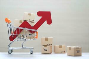 Global inflation or Deflation concept, Red arrow graph and brown parcel box on model miniature shopping cart on wooder background,Hyperinflation photo
