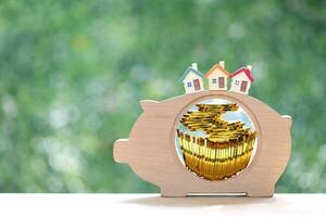 Stack of coins money in piggy bank wood and Model house on natural green background, Business investment and Real estate concept photo