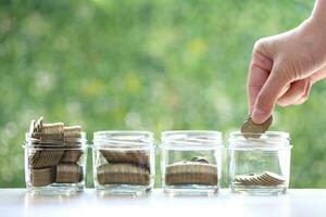 Woman hand putting a coin into the glass bottle on green background, Finance, Save money for prepare in future and pension retirement concept photo