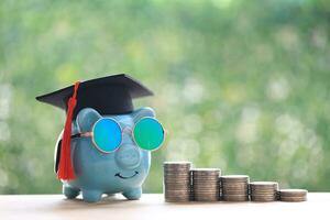 Graduation hat on piggy bank with stack of coins money on natural green background, Saving money for education concept photo