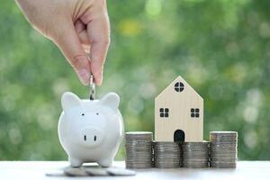 mujer mano poniendo un moneda dentro cerdito banco con modelo casa en naturaleza verde fondo, guardar dinero para preparar en futuro y familia Finanzas concepto foto