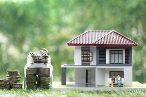 Stack of coins money in glass bottle with model house and miniature couple on natural green background, Save money for prepare in future and retirement concept photo