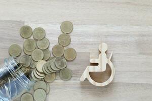 Man on wheelchair and gold coin money in the glass bottle on wooden background,Save money for prepare in future and handicapped person concept photo