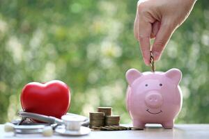 cerdito banco con estetoscopio y rojo corazón en verde fondo, guardar dinero para médico seguro y salud cuidado concepto foto