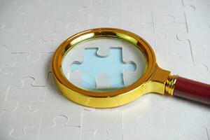 magnifying glass and on the missing puzzle piece. photo illustration concept of searching for and recruiting new employees