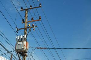 Electric pole with AC high-voltage power transformer against blue sky background photo