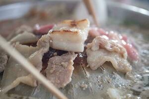 Hands are using chopsticks to grilled pork. photo