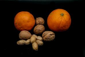 studio photo on black background of fresh and dried fruit. oranges, peanuts and walnuts in an Italian study