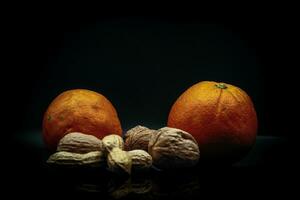 studio photo on black background of fresh and dried fruit. oranges, peanuts and walnuts in an Italian study