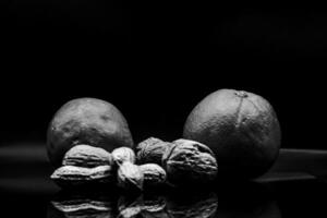 Black and white photo of fresh and dried fruits, oranges, nuts and peanuts on black background in studio