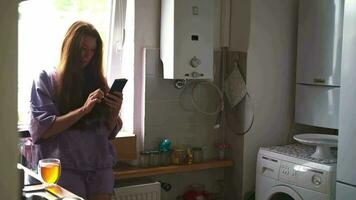 A woman in kitchen looks at her phone screen. concept of real life in a natural apartment interior video