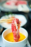 Raw sliced beef with marble texture with chopsticks and dip in raw egg. photo