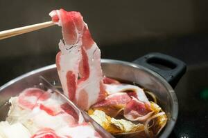 Hand holding bamboo chopsticks a piece of belly pork sliced for delicious shabu shabu photo