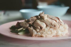 Steamed rice topped with boiled chicken and offal chicken on pink dish photo