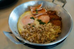 Fried eggs in a small pan with minced pork and sausages. photo