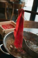 Man holding chopsticks with a piece of boiled sliced raw beef. photo