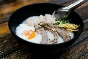 Pork chops rice porridge or congee with soft boiled egg and pork entrails in the black bowl. photo