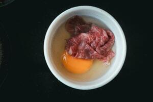 Well done slice Wagyu beef with marble texture dip in raw egg before boiling. photo