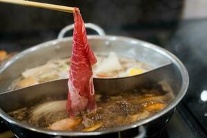 Man hand takes raw delicious beef sliced put cooking in hot boiled soup. photo