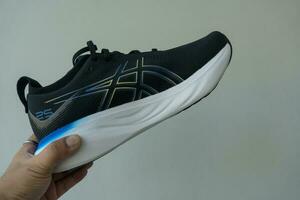 Bangkok, Thailand - January 7, 2024 Man hand holding a shoe of ASICS Running Shoes Gel Nimbus 25 WIDE. photo