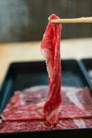 Thinly sliced raw beef cattle breed, chopsticks are picking up the beef slices. photo