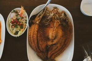 Fried sea bass fish with fish Sauce serve with spicy salad on plate photo
