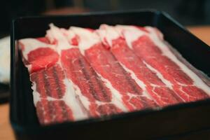 Thin beef slices for of raw thinly sliced beef served on black tray photo