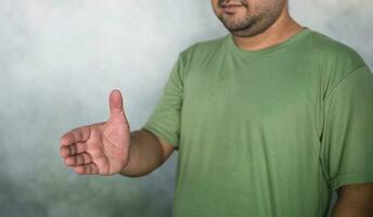 Friendly handsome bearded man wearing green T-shirt holding out his hand to side, for giving handshake photo