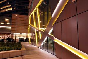 Fragment of the glass facade of a modern corporate building at night. Modern glass office  in city. Big glowing windows in modern office buildings at night, in rows of windows light shines. photo