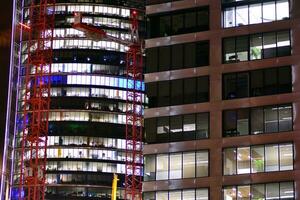 fragmento de el vaso fachada de un moderno corporativo edificio a noche. moderno vaso oficina en ciudad. grande brillante ventanas en moderno oficina edificios a noche, en filas de ventanas ligero brilla foto