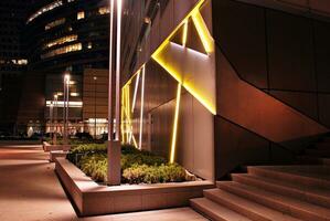 Fragment of the glass facade of a modern corporate building at night. Modern glass office  in city. Big glowing windows in modern office buildings at night, in rows of windows light shines. photo