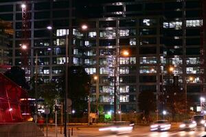 fragmento de el vaso fachada de un moderno corporativo edificio a noche. moderno vaso oficina en ciudad. grande brillante ventanas en moderno oficina edificios a noche, en filas de ventanas ligero brilla foto