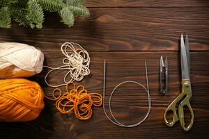 scissors, knitting needles and yarns on wooden table decorated with fir branches photo