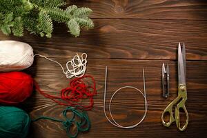 knitting needles, yarns and scissors on wooden table decorated with spruce branches photo